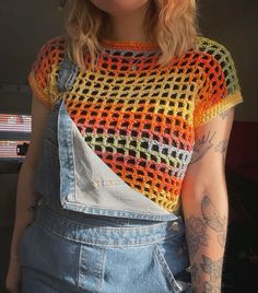 a woman wearing overalls and a crocheted top with an orange, yellow, green, and blue design