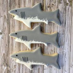 three cookies shaped like sharks with white frosting on them sitting on top of a wooden table