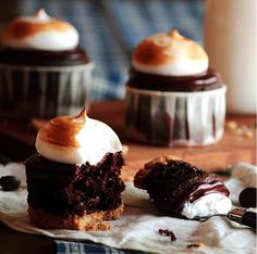 three cupcakes with chocolate frosting and marshmallows on a table