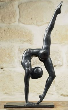 a statue of a man doing a handstand in front of a stone wall