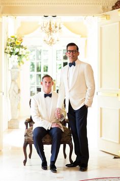 two men in tuxedos are posing for a photo inside an ornate room with chandelier