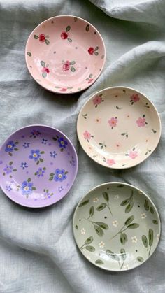 three bowls with flowers painted on them sitting on a bed sheet, one is empty and the other has no lid