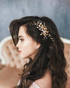 a woman with long dark hair wearing a gold head piece and pearls on it's side