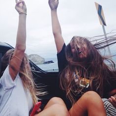 two women sitting in the back of a car with their hands up and one holding a cell phone