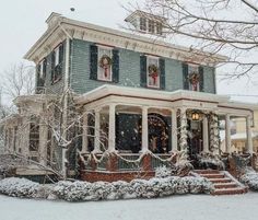 a house covered in snow with christmas wreaths on the front porch and stairs leading up to it