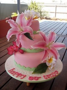 a pink and green birthday cake with flowers on the top is sitting on a wooden table