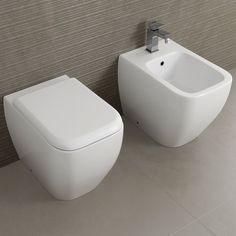 two white toilets sitting next to each other on a tiled floor in front of a wall