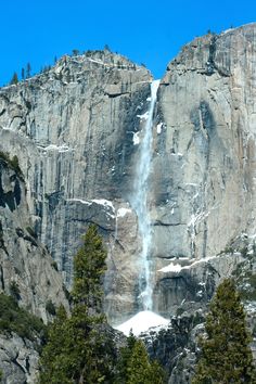 a waterfall is coming out of the side of a large rock face with trees around it