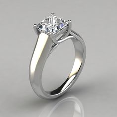 a white gold engagement ring with a princess cut diamond in the center, on a reflective surface