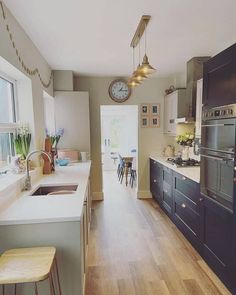 a kitchen with wooden floors and white counter tops next to a dining room table in front of a clock mounted on the wall