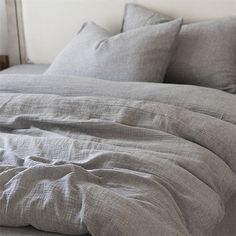 an unmade bed with grey linens and pillows