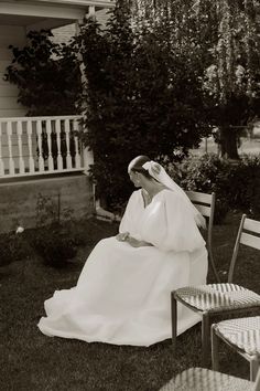 a woman sitting on top of a chair in front of a house wearing a wedding dress