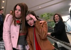 two women are standing on an escalator and one is covering her face with her hand