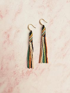 the multicolored tassel earrings are hanging from gold hooks on a marble surface