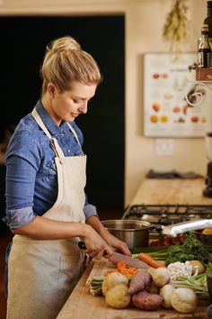 a woman in an apron chopping vegetables on a cutting board