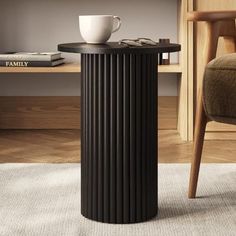 a black table with a cup on it in front of a chair and bookshelf