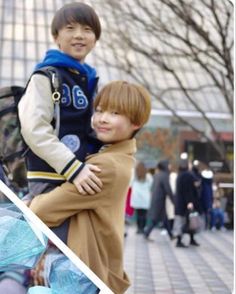 two young men standing next to each other in front of a building with people walking around