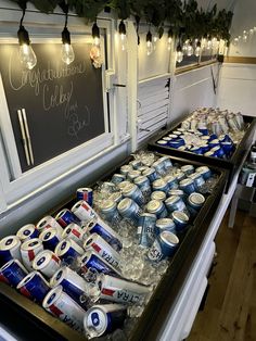 an assortment of cans and cans of beer on display in front of a chalkboard