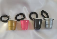 four different colored cups are lined up on a white sheet with black cords attached to them