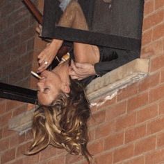 a woman is hanging upside down on the window sill with her hair blowing in the wind