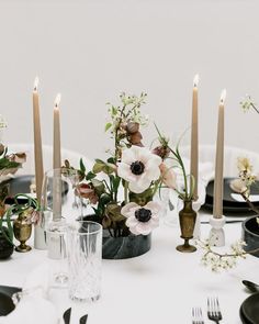 the table is set with candles and flowers in vases, plates, and silverware