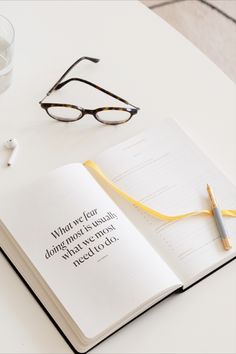 an open book sitting on top of a white table next to a pair of glasses