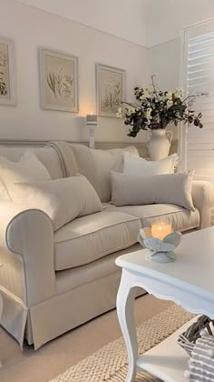 a living room filled with furniture and flowers on top of a white table in front of a window