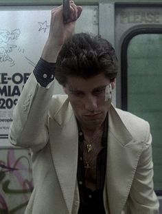 a man in a white suit holds his cell phone up to his ear while riding the subway