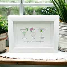 two glasses with drinks on them sitting in front of a window next to potted plants