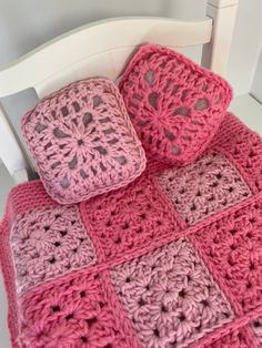 a pink crocheted blanket and two pillows on a white chair