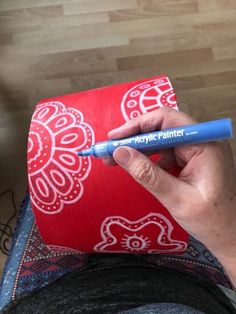 a person holding a blue marker in their left hand while sitting on the floor next to a red and white pillow