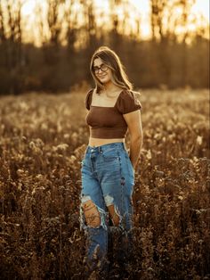 a woman standing in the middle of a field with her hands on her hips and looking at the camera