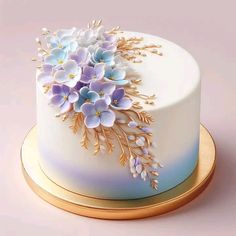 a white cake with blue and purple flowers on the top is sitting on a gold plate