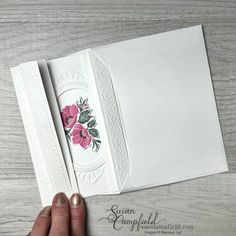 someone is holding an open white card with pink flowers on the front and back side