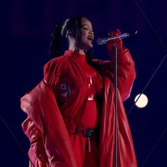 a woman in a red outfit holding a microphone and standing on stage with her hands behind her back