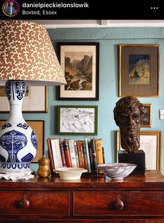 a lamp on top of a wooden table next to a dresser with pictures on the wall