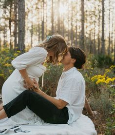 a man kneeling down next to a woman on top of a blanket in the woods