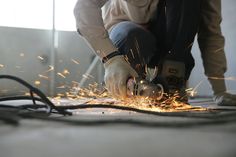 a person using a grinder to cut metal with sparks on the ground next to him