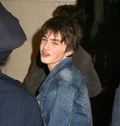 a young man wearing a jean jacket talking to someone