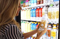 a woman is looking at some cereal in a vending machine with milk and juices behind her