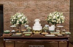 a table topped with lots of cakes and desserts next to a brick wall covered in flowers