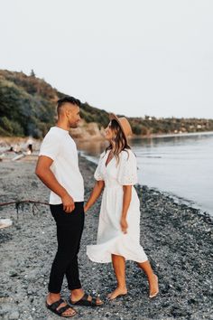 a man and woman walking on the beach next to the water holding hands with each other