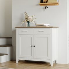 a white cabinet with two doors and drawers next to some stairs in a room that has wood flooring