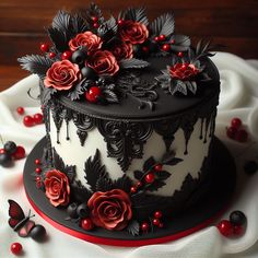 a black and white cake with red flowers on top, surrounded by berries and leaves