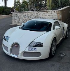 a white bugatti parked in front of a stone wall