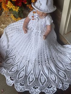 a white crocheted dress and hat is on display in front of some flowers