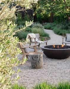 an outdoor fire pit surrounded by wooden chairs and tables in the middle of a gravel path