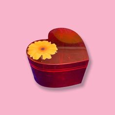 a heart shaped box with a yellow flower in it's center on a pink background