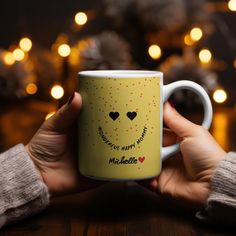 a person holding a yellow coffee mug with hearts on it