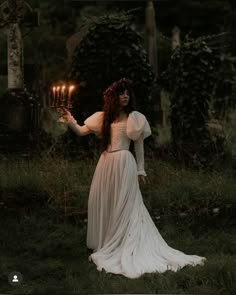 a woman in a white dress holding two candles